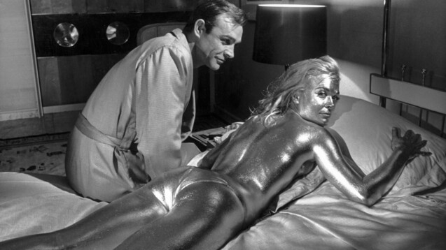 Sean Connery als James Bond und die goldüberzogene Shirley Eaton als Jill: aufgenommen während der Dreharbeiten zu „Goldfinger" 1964. (p / Foto: picture alliance/KEYSTONE | STR)